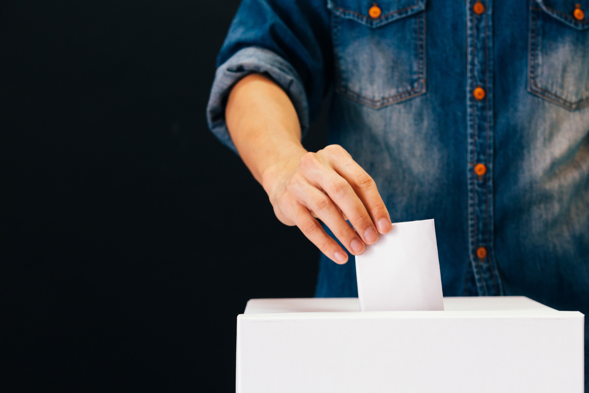 Front view of person holding ballot paper casting vote at a polling station for election vote in black background Front view of person holding ballot paper casting vote at a polling station for election vote in black background