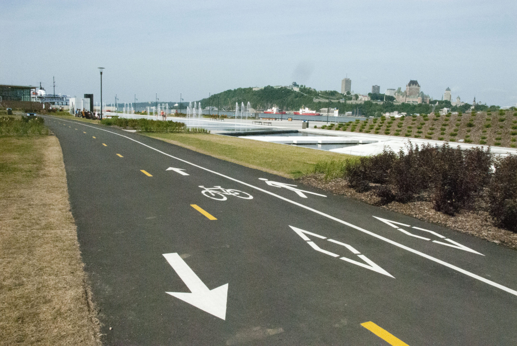 Une piste cyclable bien aménagée le long d'un plan d'eau. On peut voir des marquages au sol indiquant les directions pour les cyclistes et les piétons.